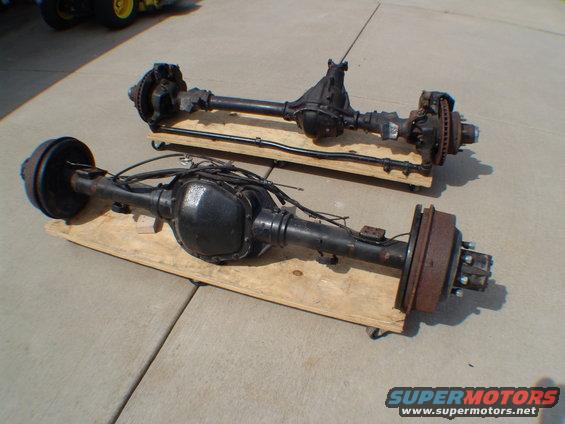 Two black vehicle rear axles on wooden dollies, one with drum brakes, the other with disc brakes