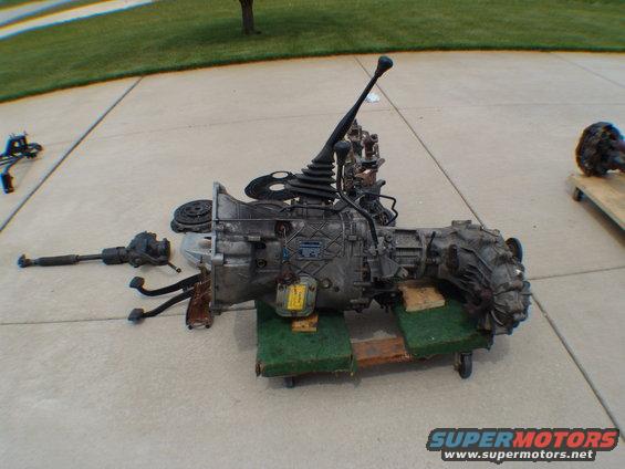 Transmission and driveshaft assembly on green padding, with another differential visible on a wooden dolly