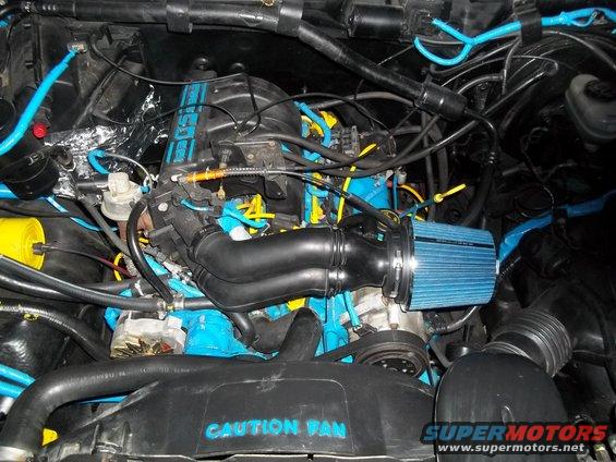 Engine bay with blue and yellow accents, a blue cone air filter and black intake piping