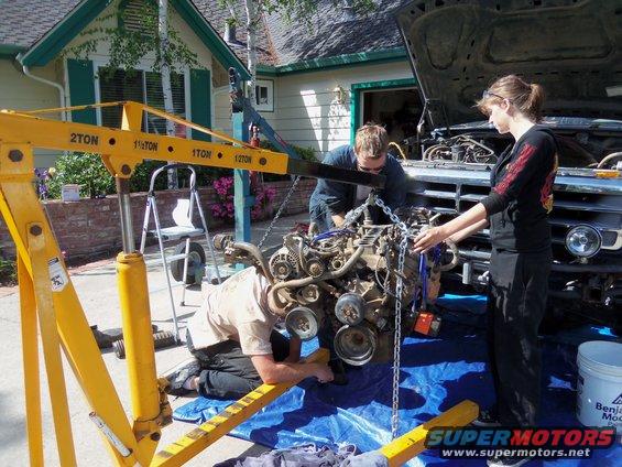 Engine being lifted out of a truck with an engine hoist; two people are guiding it