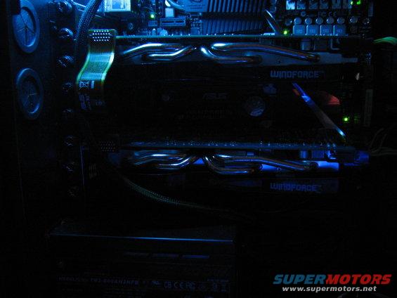 Computer internal components with blue LED lighting. Two graphics cards with 'WINDFORCE' branding are visible