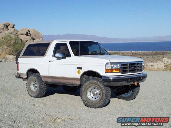 White Ford Bronco parked on dirt road with mountains and a body of water in the background