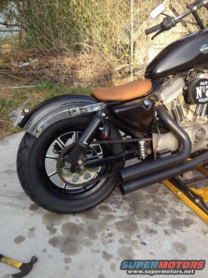 Side view of a black Harley-Davidson motorcycle with a brown seat and dual exhaust pipes. It's on a yellow stand