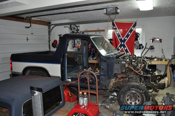 Pickup truck with front end removed, parked in a garage with tools and a Confederate flag