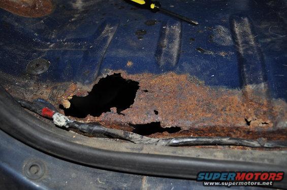 Rusted blue floor pan with large hole and wiring harness