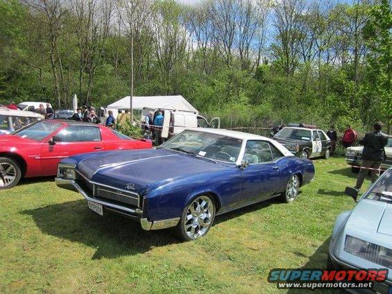 Blue 1967 Buick Riviera coupe with a white roof and chrome wheels parked on grass