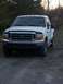 2000 Ford F-250 - A white Ford F-250 truck is parked on a gravel surface with trees in the background.