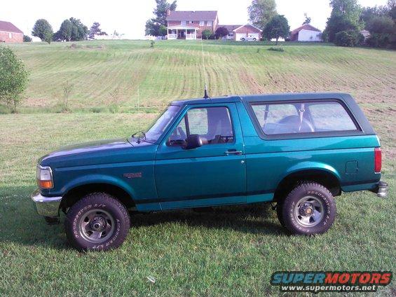 Green 1996 Ford Bronco parked on grass with houses and hills in background
