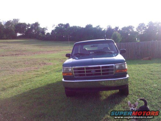 Green Ford Bronco with chrome grille, parked on grass in front of a wooden fence