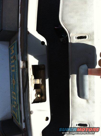 Close-up of a car's interior door latch mechanism and panel, with a partial view of a license plate