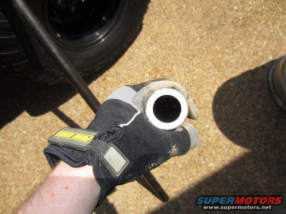 gloved hand holding a metal tube, with a tire and part of a car visible in background