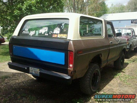 Rear view of a brown 1978 Ford Bronco with a tan top and a blue panel on the tailgate. Another vehicle is parked behind it