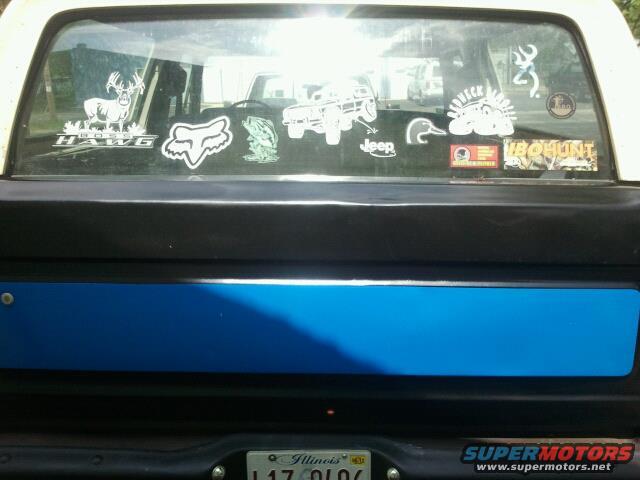 Rear window of a truck covered in stickers like a deer, fox logo, and Jeep. Blue stripe below