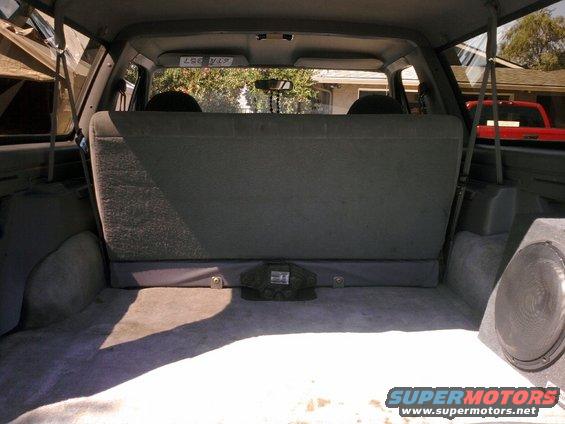 Back cargo area of an SUV with folded-down rear seats, a speaker box on the right, and a red truck visible through the rear window