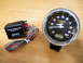 2004 Ford Crown Victoria - A tachometer and its adapter are displayed on a wooden surface, ready for installation.