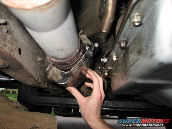 hand holding a metal clamp around a vehicle's exhaust pipe