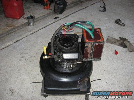 Modified lawnmower engine with a custom metal fuel tank and hoses attached