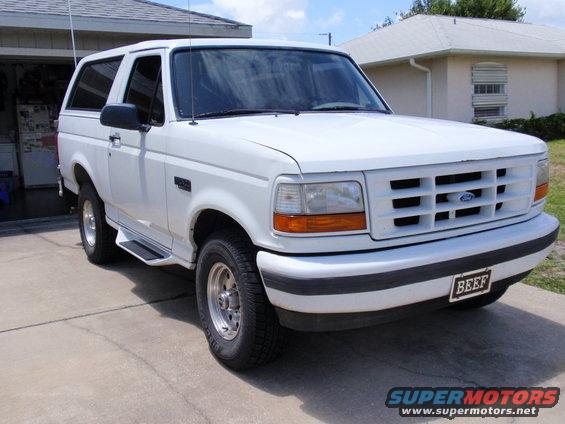 White Ford Bronco SUV parked in driveway, front 3/4 view. License plate reads 'BEEF'