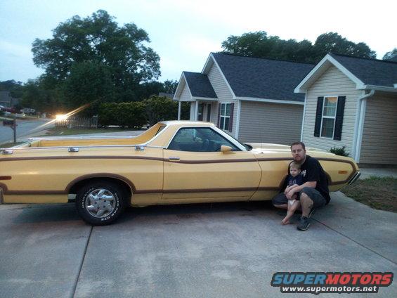 Man and child squatting next to a yellow 1974 Ford Ranchero
