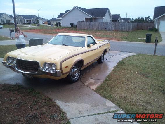 Yellow 1972 Ford Ranchero with brown side trim parked on a wet driveway