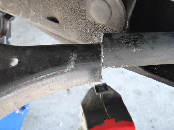 Close-up of a cut metal suspension arm with rough edges, held by red and black pliers