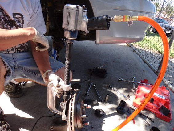 Impact wrench and ball joint separator tool working on car suspension part. Tools and red toolbox on ground