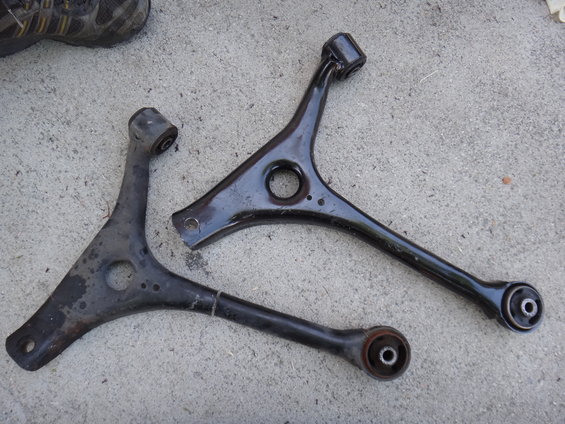 Two black metal control arms with rubber bushings on a concrete surface