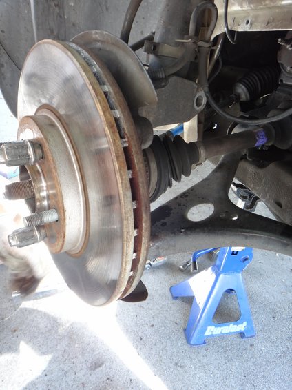 Close-up of a car's front brake rotor and suspension components, with a blue jack stand visible