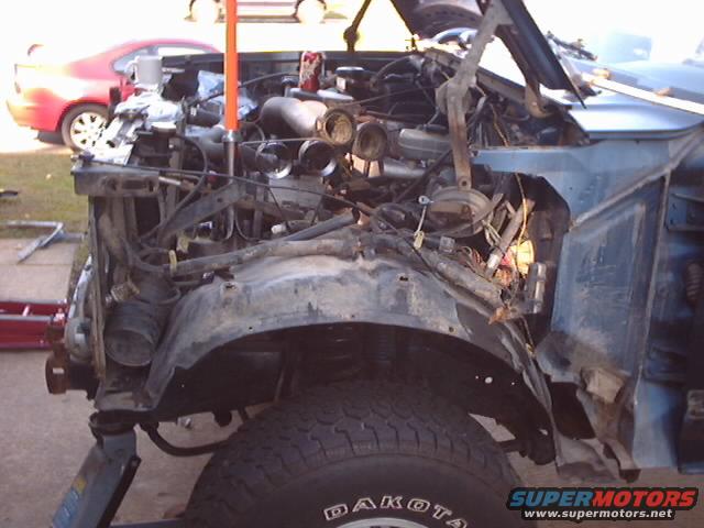Blue 1990 Ford Bronco front end with damaged bodywork and exposed engine components
