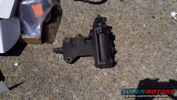 Black steering gear box with mounting holes and input shaft, on concrete
