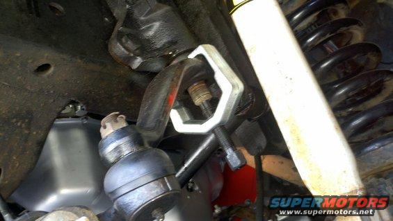 Tie rod end removal tool attached to vehicle suspension components