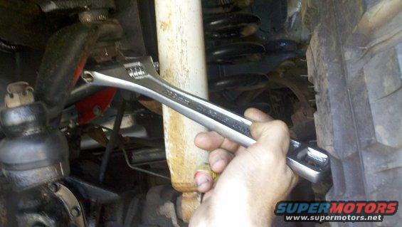 Hand using adjustable wrench on vehicle suspension near shock absorber and ball joint