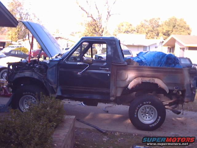1990 Ford Bronco with hood open, engine removed, and bed covered with a blue tarp