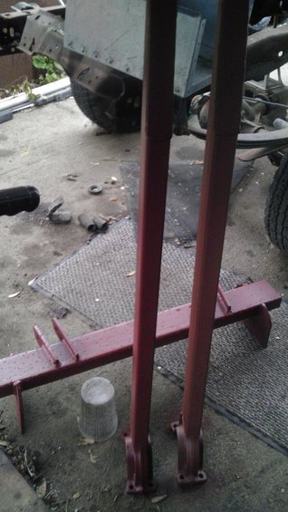 Vehicle frame with suspension components and red painted metal parts on the ground