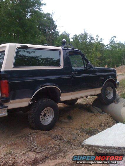 1992 Ford Bronco side view, dark blue and tan, off-roading over rocks