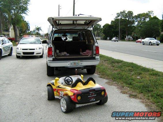 Yellow toy car and white SUV with open trunk parked on asphalt