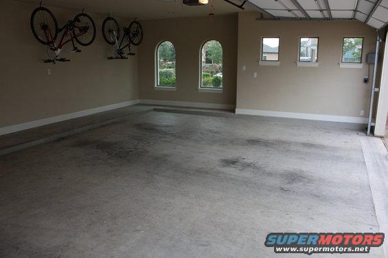 Empty garage interior with two bicycles hanging from ceiling mounts. Three arched windows and three rectangular windows are visible