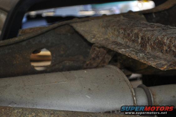 Close-up of heavily rusted vehicle frame and exhaust pipe. Supermotors.net logo visible