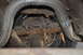 1986 Ford Bronco - Underside view of a heavily rusted rear axle and exhaust system, showing leaf springs and a differential housing.