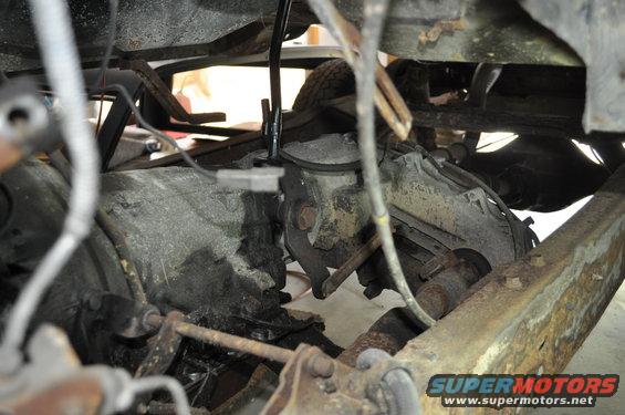 Undercarriage view of a vehicle showing transmission, driveshaft, and suspension parts. Some rust is visible on the frame