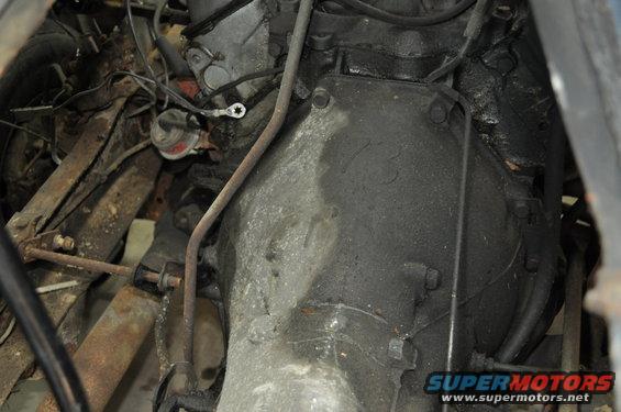 Engine and transmission assembly with oil and grime, showing various metal parts and wiring