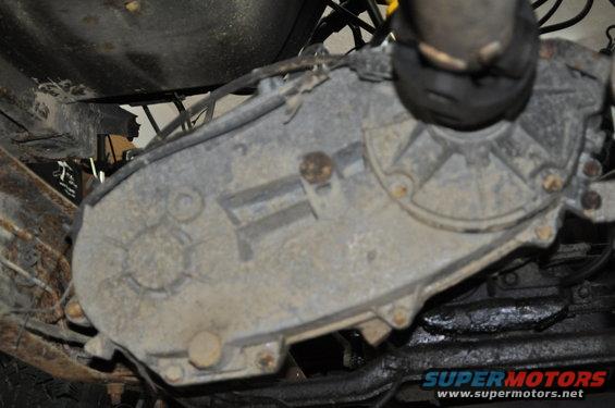 Underside view of a dirty transfer case with bolts and hoses attached