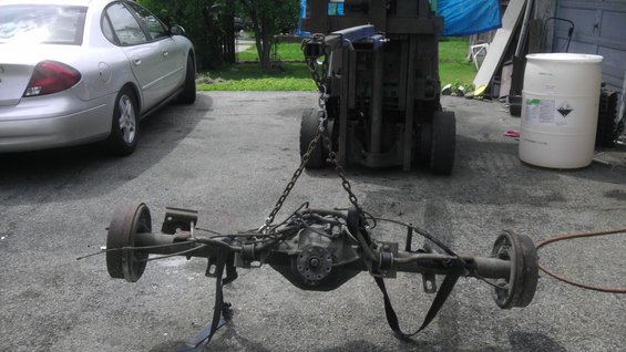 Rear axle assembly with drum brakes, suspended by chains from a forklift