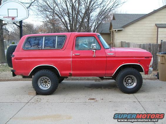 Red Ford Bronco parked on driveway, side view. Spare tire mounted on rear