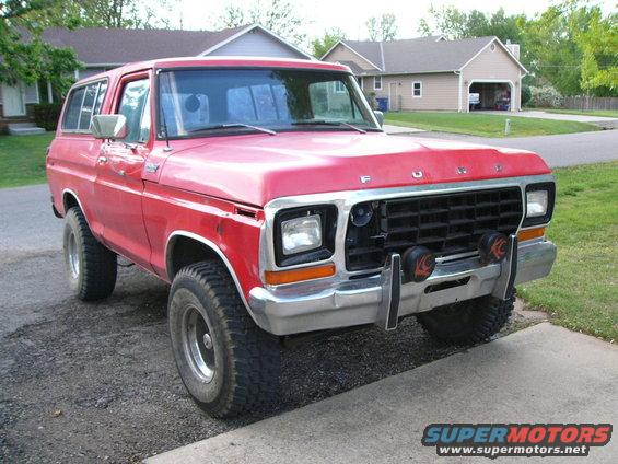 Red Ford Bronco parked in a driveway. It has a black grille and chrome bumper