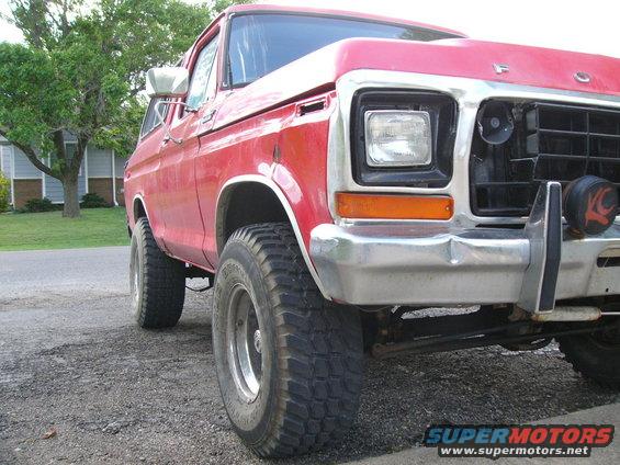 Red Ford Bronco with chrome bumper and off-road tires, viewed from a low angle