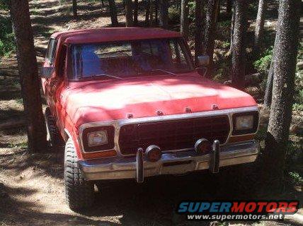 Red 1978 Ford Bronco with chrome bumper and auxiliary lights parked on a dirt path in a forest