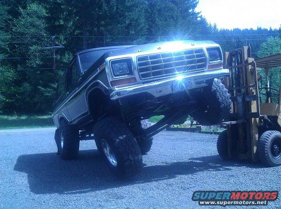 Lifted 1978 Ford Bronco front end held by a yellow forklift