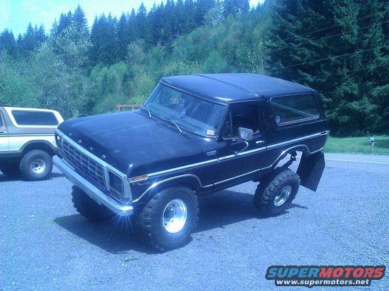 Black lifted Ford Bronco parked next to a tan Bronco. Lifted Bronco has large tires and chrome wheels