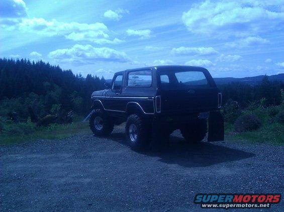 Black Ford Bronco lifted with large tires, parked on a gravel road with trees and sky in background